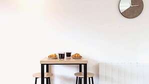 Un comedor minimalista con una mesa de madera, dos taburetes negros, un reloj en la pared y un radiador.