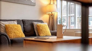 Una sala de estar moderna con un sofá gris oscuro, dos cojines amarillo mostaza, una mesa de centro de madera y una lámpara de pie.