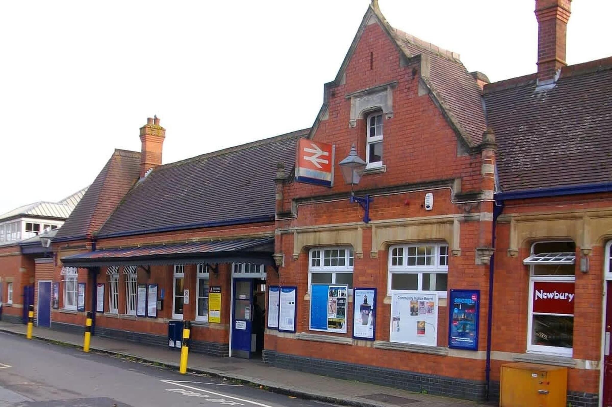A red brick building with a traditional architectural style, featuring a prominent flag and multiple windows displaying various notices.