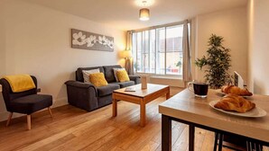 Una sala de estar moderna con un sofá, una mesa de centro, una mesa de comedor con croissants, una taza de café y una planta en maceta.