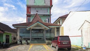 A building with a green and red facade, a tiled roof, and a parked red car in front.