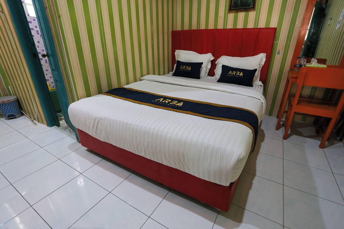 Una habitación de hotel con una cama grande, papel tapiz a rayas y un cabecero rojo.