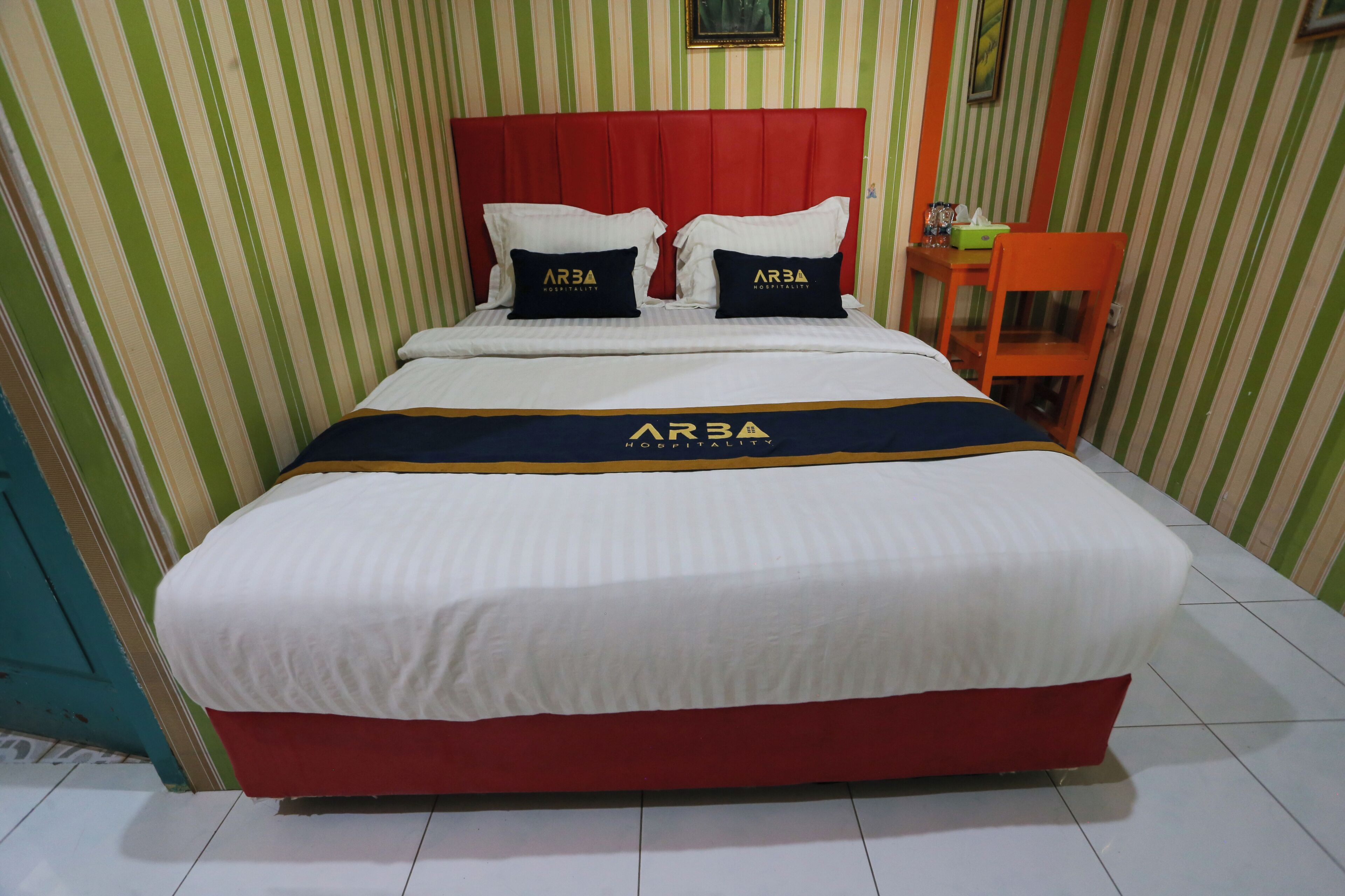 A bed with a red headboard, white bedding, and two pillows with 'ARBA' branding.