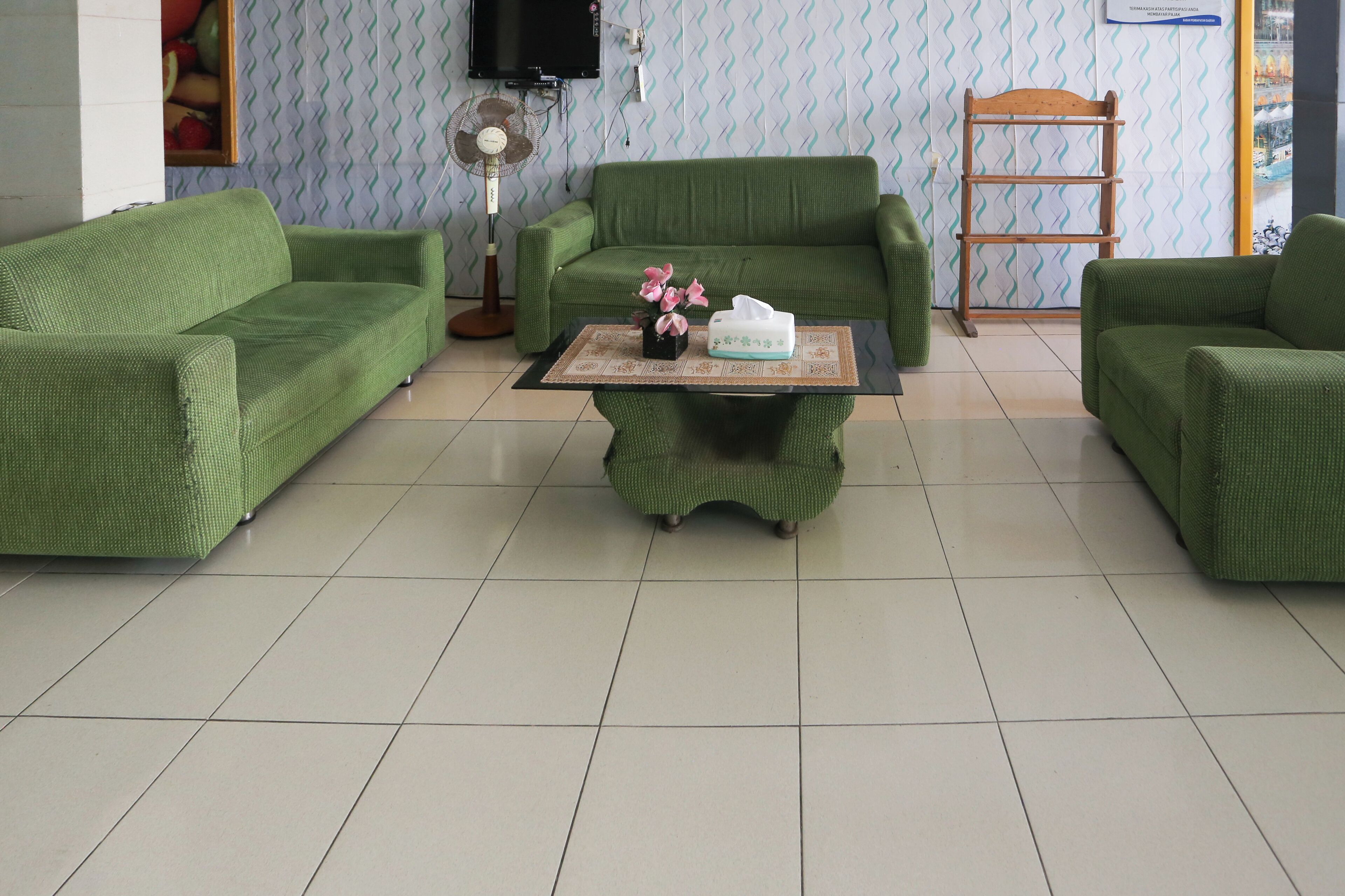 A green-themed living room with a sofa set, a coffee table with a vase of flowers, and a television on the wall.