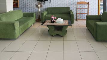 A green-themed living room with a sofa set, a coffee table with a vase of flowers, and a television on the wall.