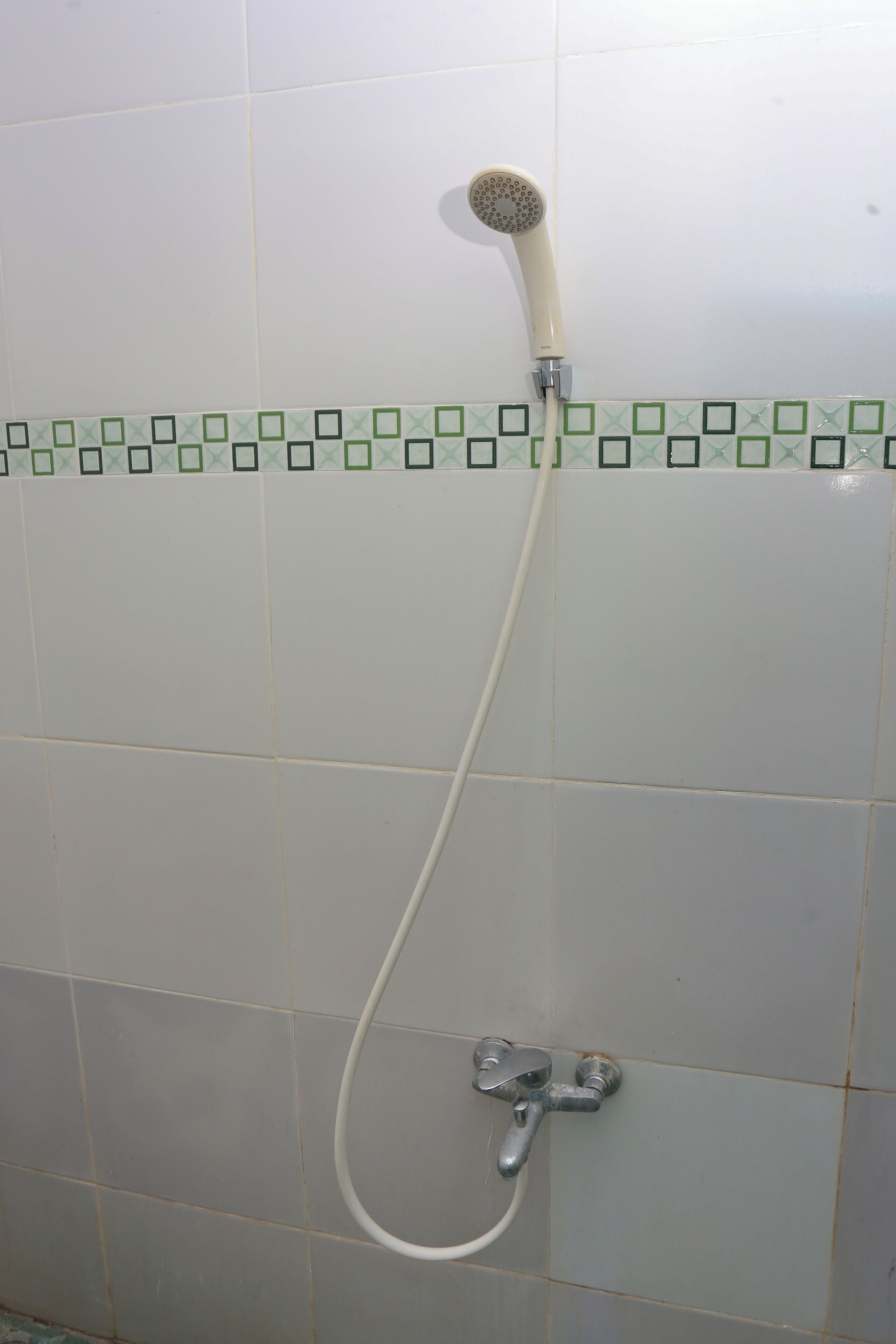 Une douche équipée d’un pommeau de douche à main et d’un robinet fixé au mur.