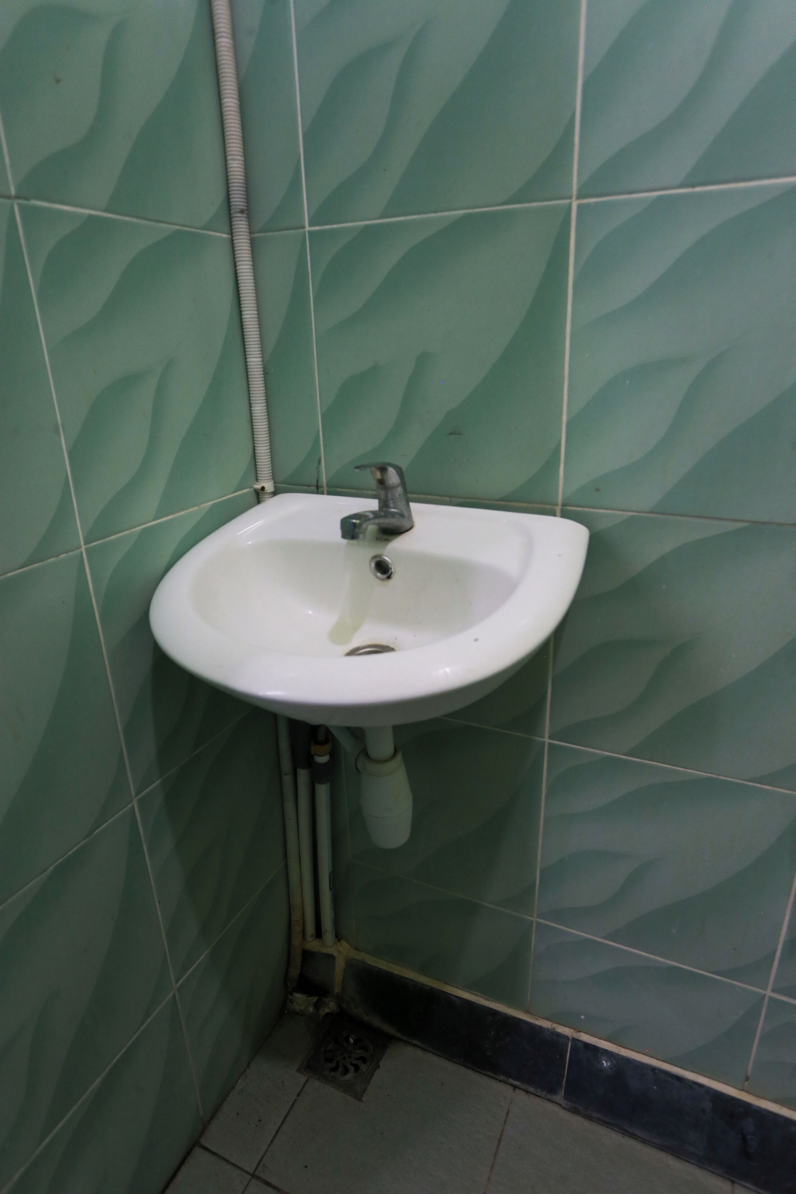 A bathroom with a white sink, green patterned tiles, and a visible drainpipe.