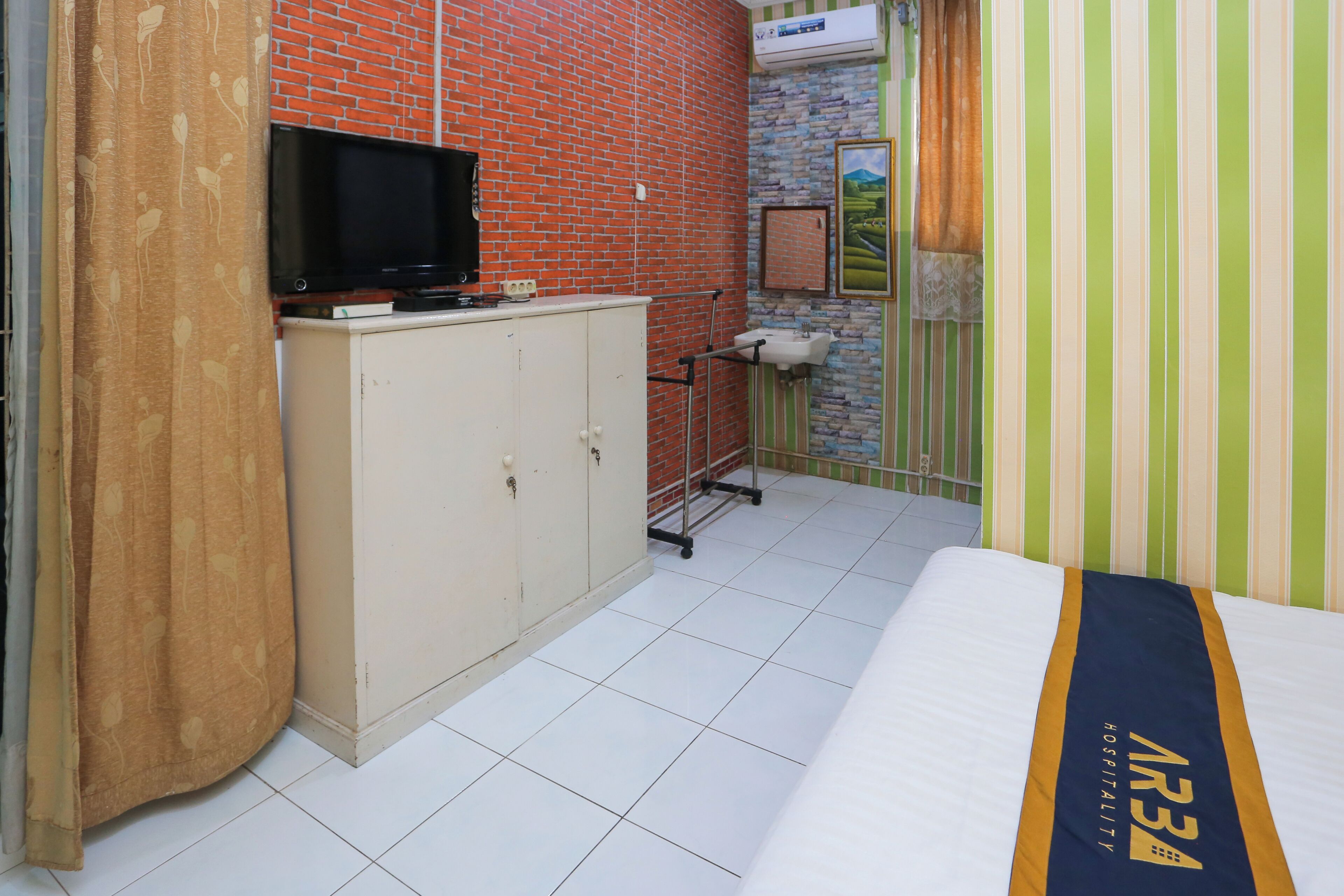Habitación de hotel con pared de ladrillo, televisor sobre un mueble, lavamanos y cama junto a una pared a rayas.