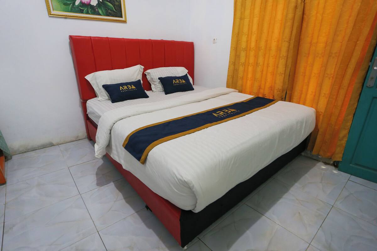 Una cama con cabecera roja, ropa de cama blanca y una colcha azul y dorada.