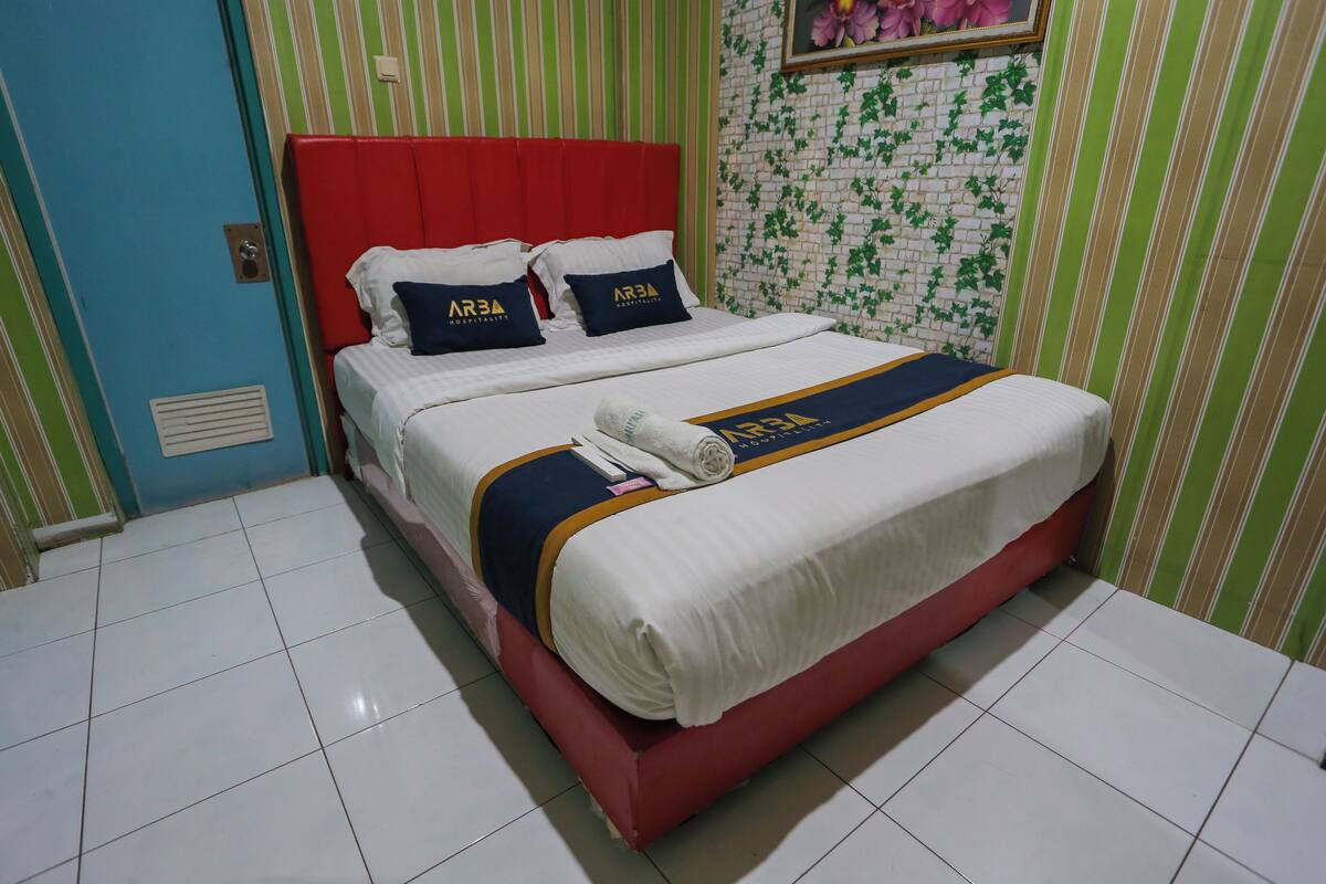 Habitación de hotel con cabecera roja, ropa de cama blanca y pared verde y blanca a rayas.