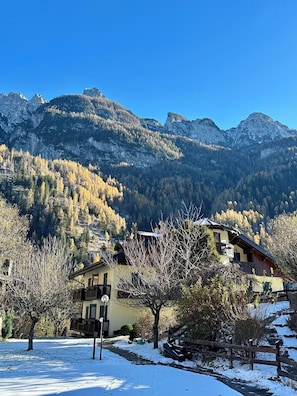 A mountain cabin with a balcony, surrounded by snow-covered ground and trees, with a clear view of the mountains in the background. - Dolomites Soundscape Apartment Alleghe (Rocca Pietore)