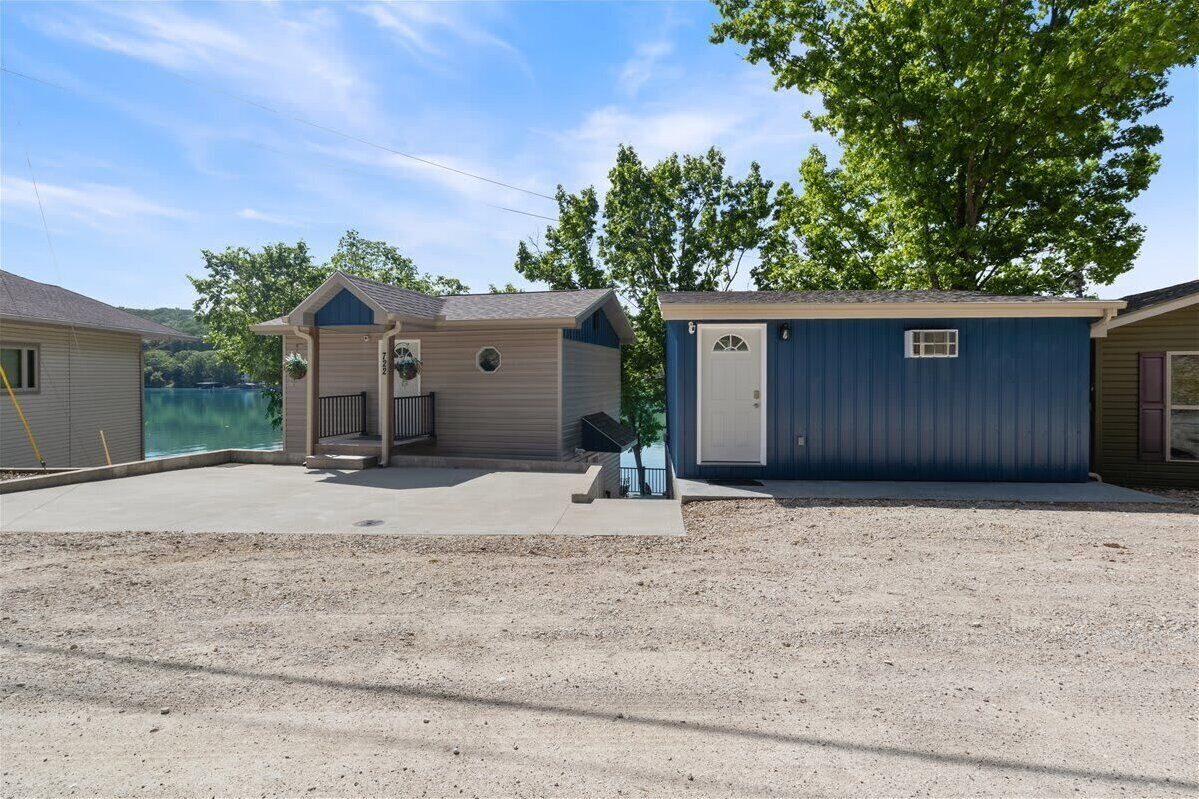 A small, single-story building with a garage, a covered porch, and a small outdoor seating area.