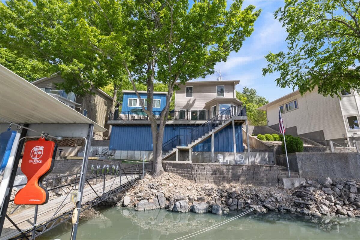 Una propiedad frente al agua con un muelle, una escalera que conduce a un edificio azul y un muro de piedra.