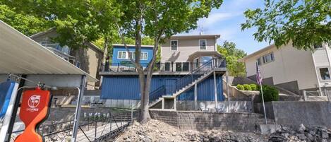 Una propiedad frente al agua con un muelle, una escalera que conduce a un edificio azul y un muro de piedra.