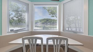 A corner room with a dining table and chairs, large windows with blinds, and a paddle on the wall. - Lakeside Serenity Dock Days & Firepit Nights (Gravois Mills)