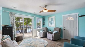 A living room with teal walls, a ceiling fan, a large window, and a sliding glass door leading to a balcony. - Lakeside Serenity Dock Days & Firepit Nights (Gravois Mills)
