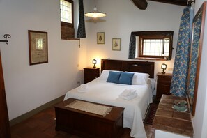 Ein Schlafzimmer mit einem großen Bett, einem Holz-Kopfteil, Nachttischen mit Lampen, einer kleinen Bank und einem Fenster mit Vorhängen.