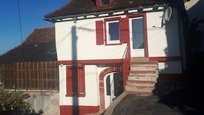 Une maison à deux étages avec une façade rouge et blanche, une cheminée et une petite fenêtre.