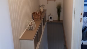Un couloir étroit avec un banc en bois, une petite table ornée de quelques objets décoratifs, un miroir et une porte donnant sur une autre pièce.