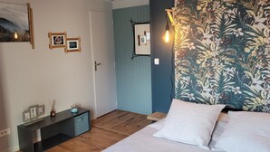 Une chambre à coucher comprenant un lit, une table de chevet, une commode, une porte et un mur recouvert d’un papier peint à motifs floraux.