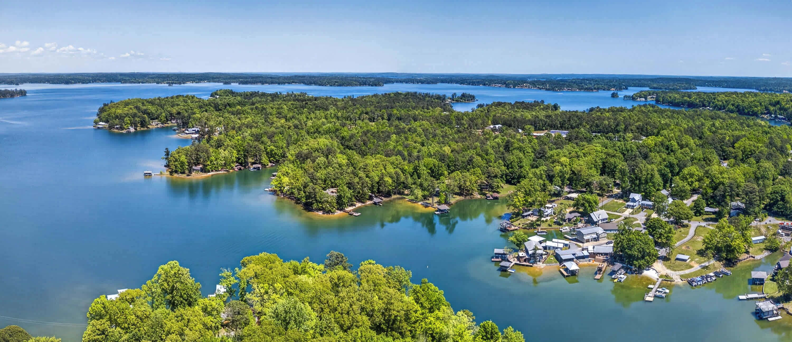 An aerial view of a lakeside property with multiple docks, a marina, and a cluster of buildings surrounded by dense forest.