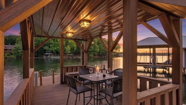 Una terraza de madera con una mesa y sillas, con vista a una masa de agua con barcos y un muelle.