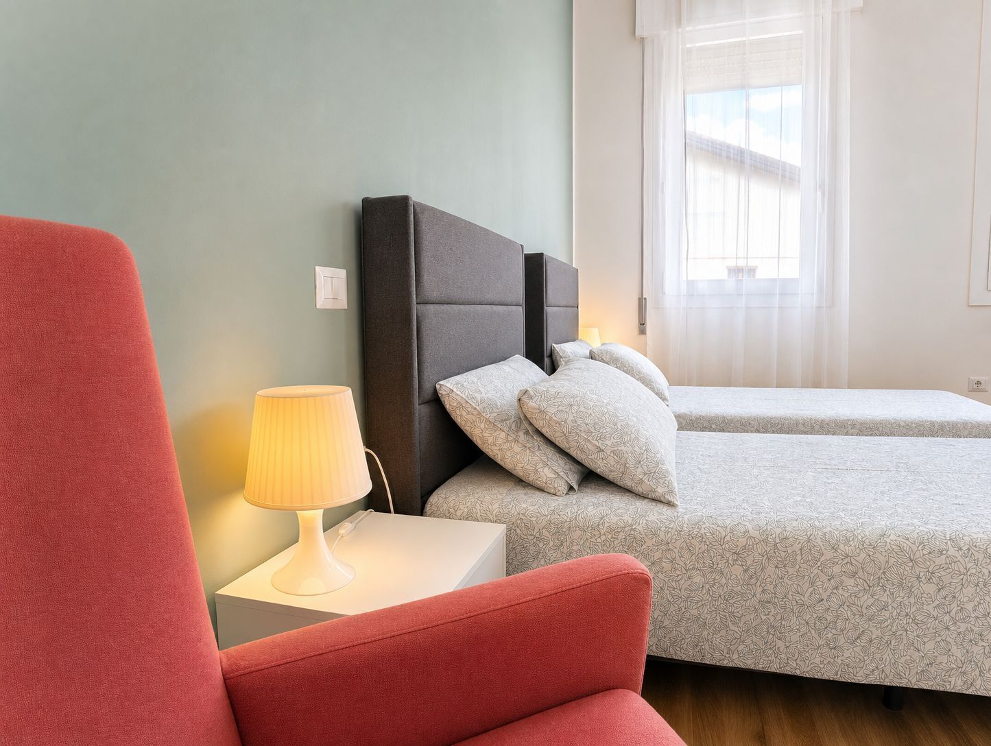 A room with a bed, a nightstand with a lamp, and a red chair.