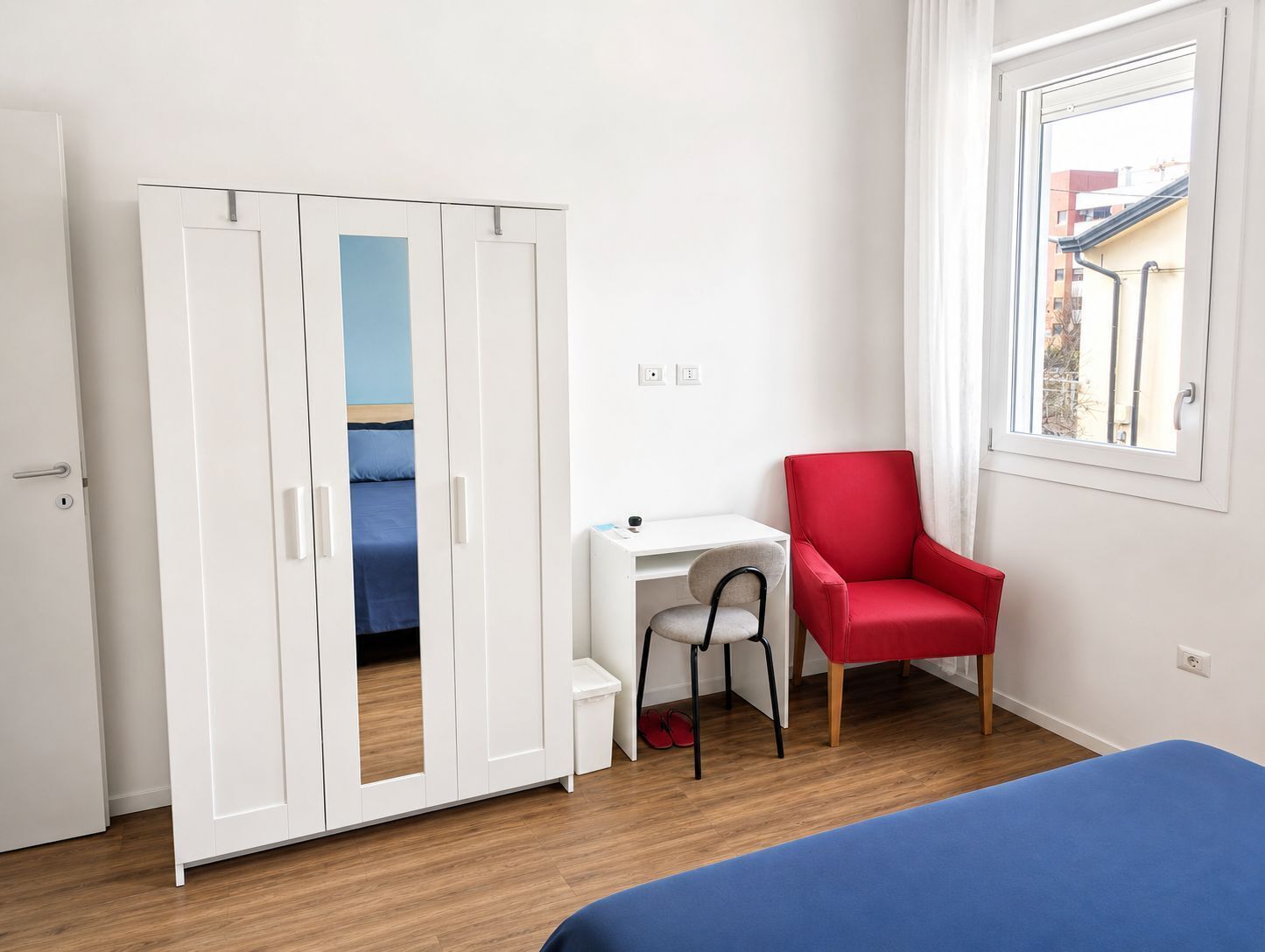 A room with a bed, a desk, a red chair, and a wardrobe.