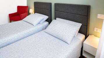 Un lit simple avec une tête de lit grise, une chaise rouge et une table de chevet avec une lampe.