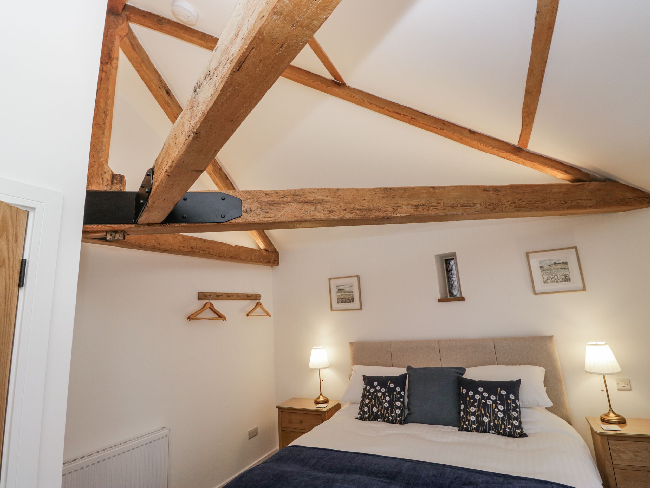 Une chambre avec des poutres apparentes, un lit avec deux oreillers, des lampes de chevet et une petite fenêtre.