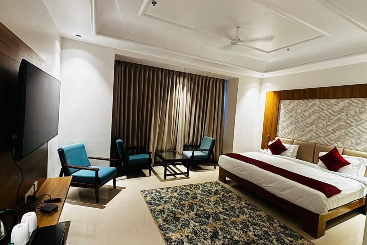 Ein Hotelzimmer mit einem großen Bett, einem Fernseher, einem Schreibtisch mit Wasserkocher und zwei Sesseln.