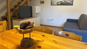 A wooden dining table with a pine cone centerpiece, a wooden chair, a blue sofa, and a staircase in the background. - Natalia Cottage (Pieve di Ledro)