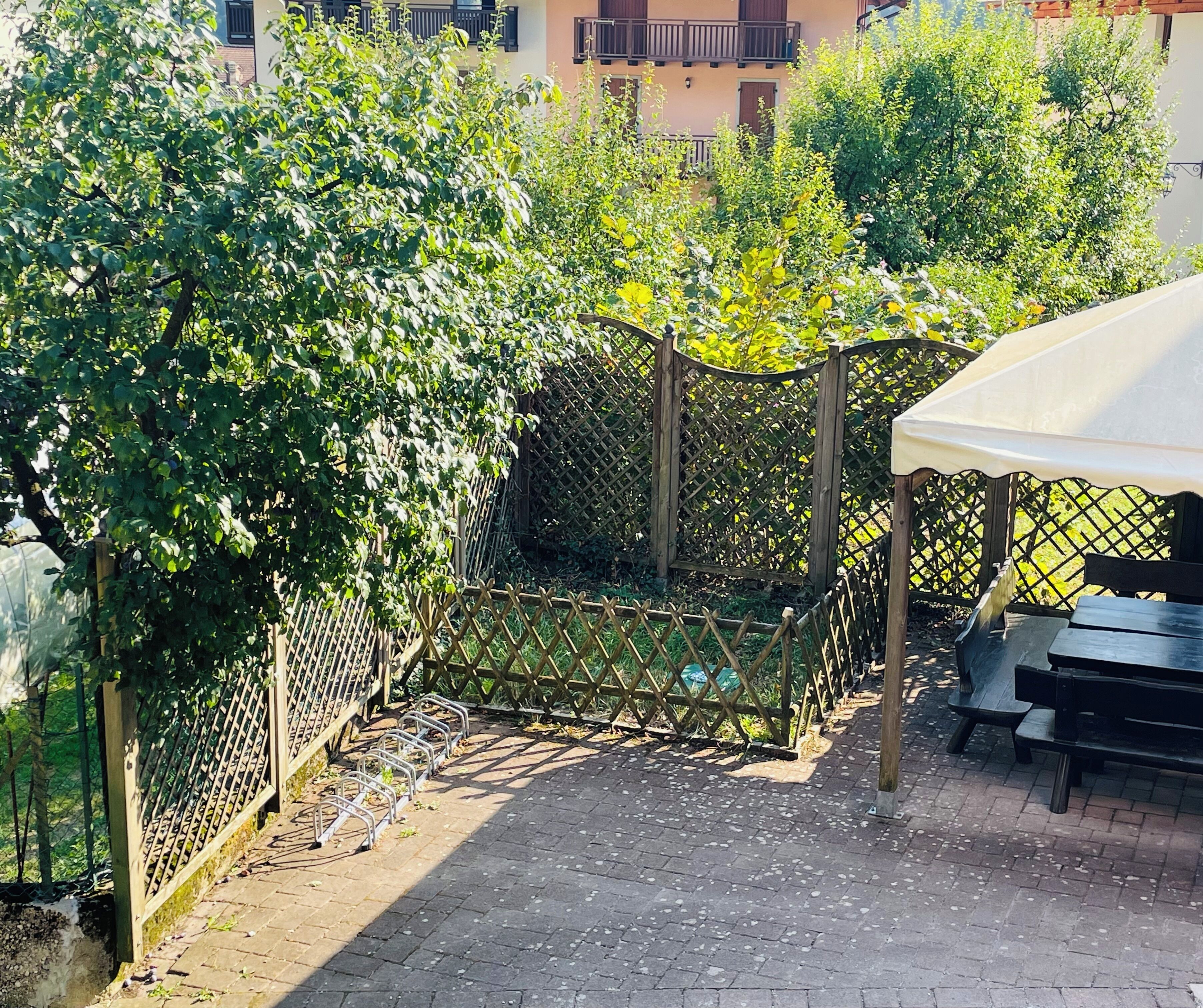 En trädgårdsdel med en pergola, sittplatser och ett staket.