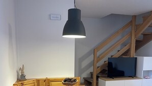 A wooden dining table with benches, a black pendant light, and a television on a cabinet. - Natalia Cottage (Pieve di Ledro)