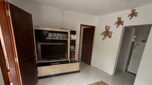 Un'ampia stanza con un grande tappeto, un mobiletto a incasso per l'intrattenimento e una porta che conduce in un'altra zona.