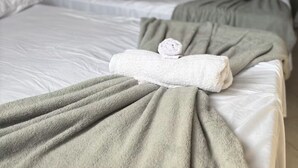 Una camera d'albergo con letti multipli, ognuno con un asciugamano piegato e una coperta.