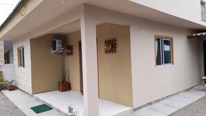 Un edificio a due piani con un portico coperto, un piccolo giardino con una pianta in vaso e un elemento decorativo a parete.