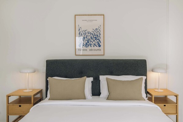 A neatly made bed with two pillows, a framed artwork above, and two bedside tables with lamps.