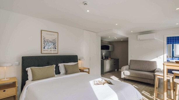 Habitación de hotel moderna con una cama grande, un escritorio, una silla y una kitchenette al fondo.