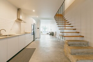 Una cocina moderna con armarios blancos, una campana extractora de acero inoxidable y una escalera de madera con escalones de piedra que conducen a una sala de estar.