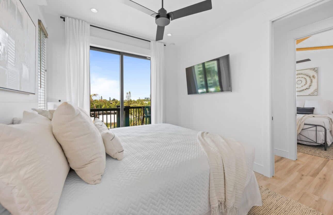 Une chambre dotée d’un grand lit, d’un ventilateur de plafond, d’une télévision et d’un balcon offrant une vue sur la verdure.