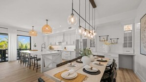 A modern kitchen with white cabinetry, a central island, pendant lighting, and a dining area set for six.
