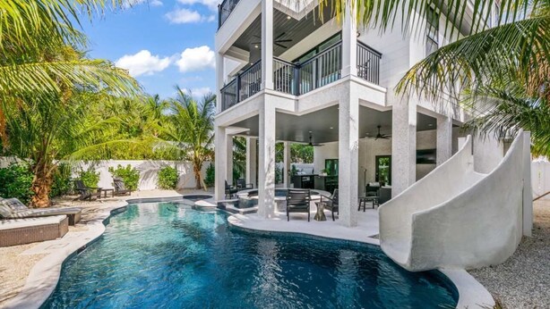 A modern multi-story building with a pool, outdoor seating, and palm trees.