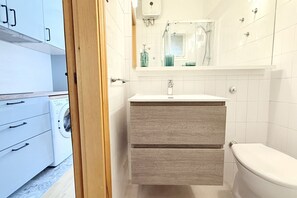 Ein kleines Badezimmer mit Toilette und Waschbecken, eine Waschmaschine befindet sich im angrenzenden Raum.