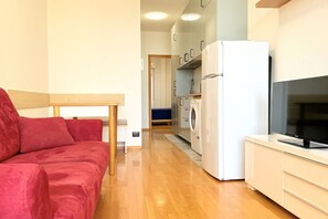 Ein kompakter Wohnraum mit Sofa, Waschmaschine, Kühlschrank und Fernseher.
