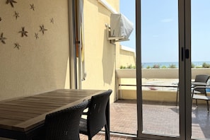 Ein Balkon mit Tisch und Stühlen, eine Schiebetür und Blick aufs Meer.