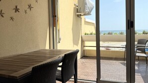 En balkon med et bord og stole, en skydedør samt havudsigt.