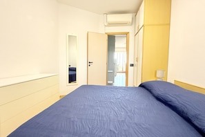 Une chambre à coucher avec un lit, une porte, un miroir et un climatiseur fixé au mur.