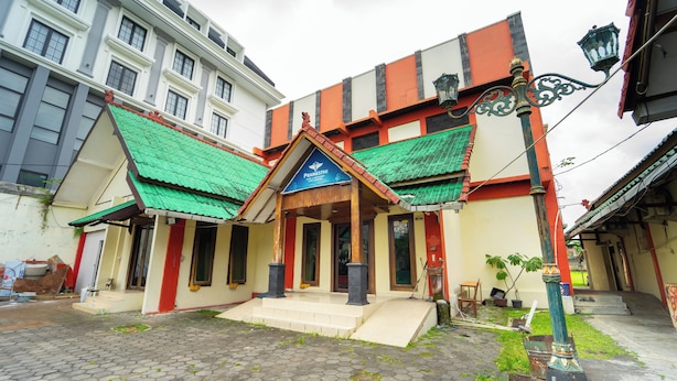 Un bâtiment traditionnel doté d’un toit végétalisé, d’une enseigne portant l’inscription « Pramesthi » et d’une cour pavée.