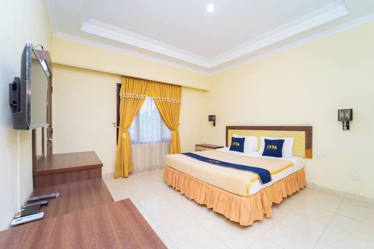 Une chambre d’hôtel avec un grand lit, une télévision, un bureau et une fenêtre avec des rideaux.